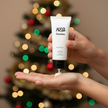 Hydrating hand cream being applied to a hand, with a festive background of colored lights and a Christmas tree.