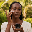 Model applying hyaluronic moisturizer cream to her face in a lush outdoor setting.