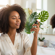 Woman applying makeup setting spray in a bright bathroom with plants in the background.