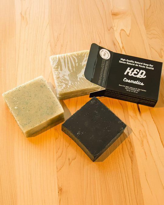 Natural soap bars including activated charcoal soap by KED Cosmetics on a wooden surface.